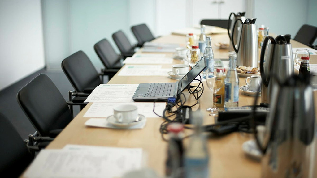 Image of a conference table with a laptop, printed documents and beverages